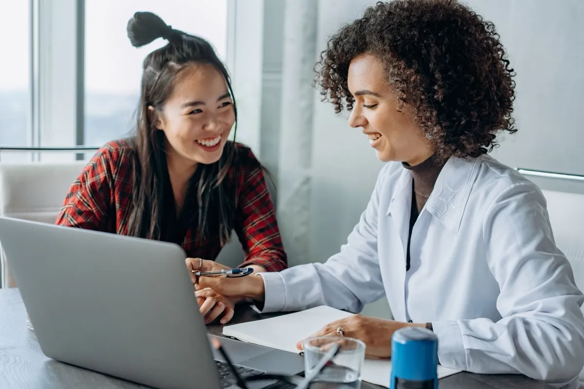 Two colleagues laughing together as they work on a laptop at a shared desk