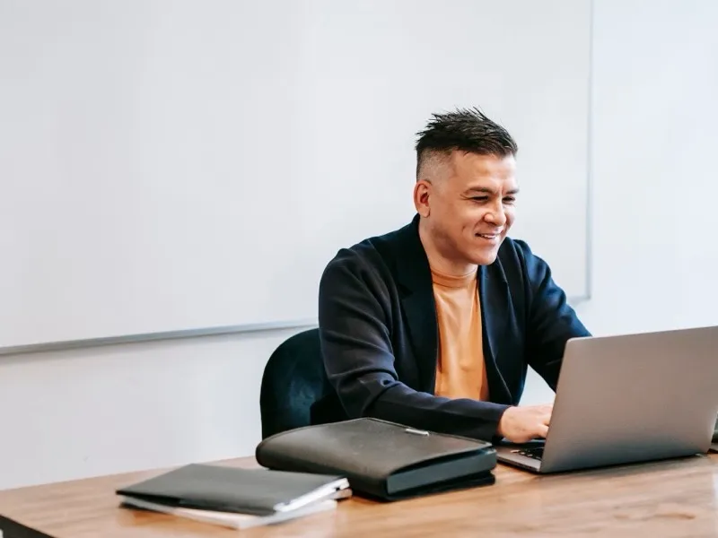 A man smiling as he works on his laptop at an office desk