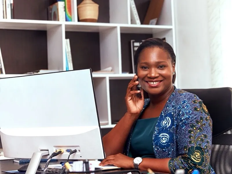 A receptionist smiling as she takes a call at her desk, with her computer beside her