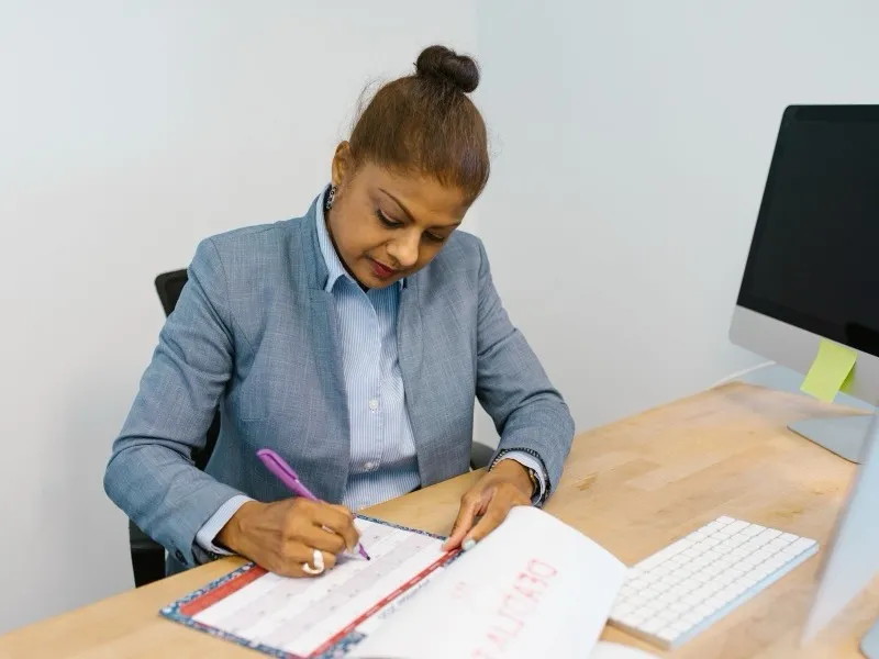 A woman in a grey blazer writing in a calendar at her office desk
